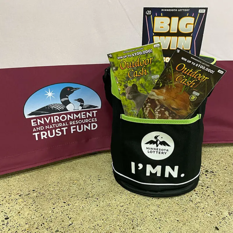 Minnesota Lottery bag with three scratch-off tickets in front of Environment and Natural Resources Trust Fund sign with loon logo.
