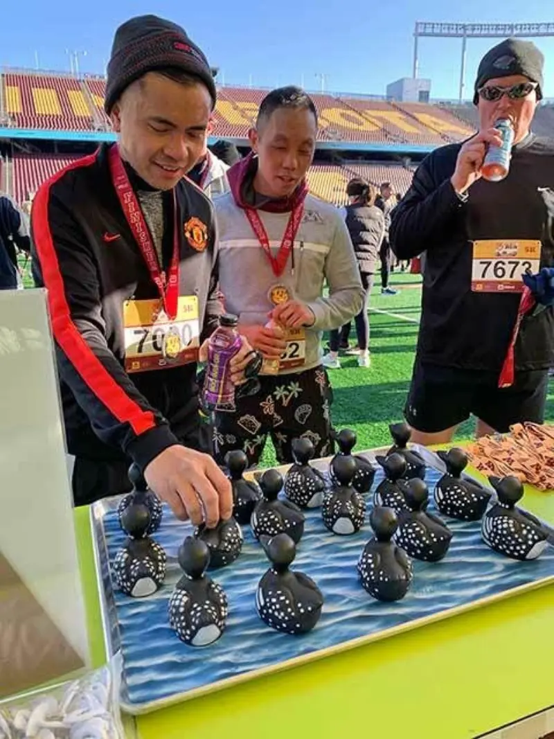 Two men in race attire examine decorated rubber ducks on a table, related to Minnesota State Lottery's Scratch Games and 2nd Chance program.