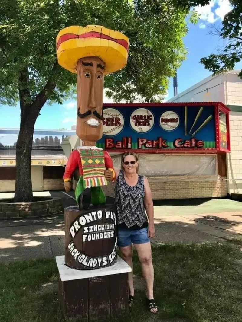 Woman in sunglasses and summer clothes stands by a large, colorful statue of a man in a sombrero outside Ball Park Cafe.