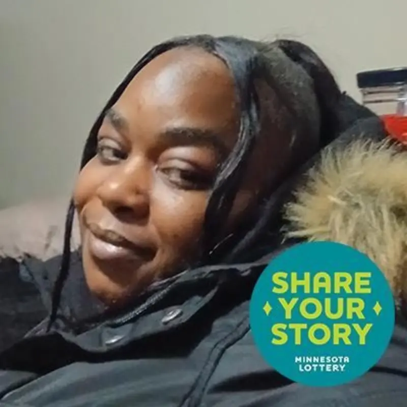 Smiling person in a dark fur-lined coat reclines indoors. A "SHARE YOUR STORY MINNESOTA LOTTERY" sticker appears at bottom right.