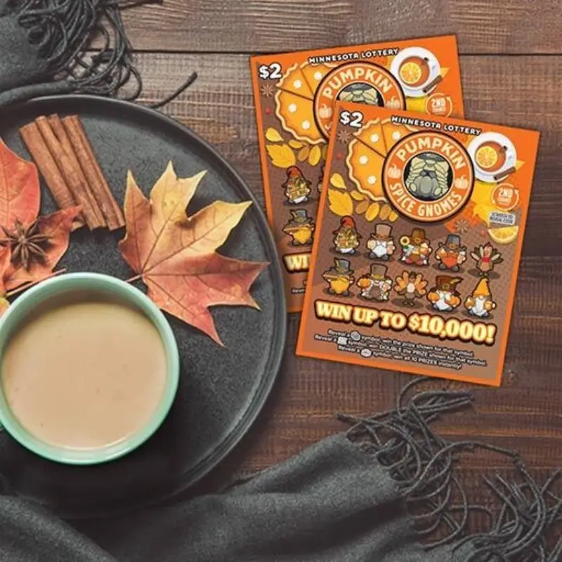 Coffee on a plate with spices and leaves beside two Pumpkin Spice Gnomes scratch-off tickets on a wooden table with dark cloth.