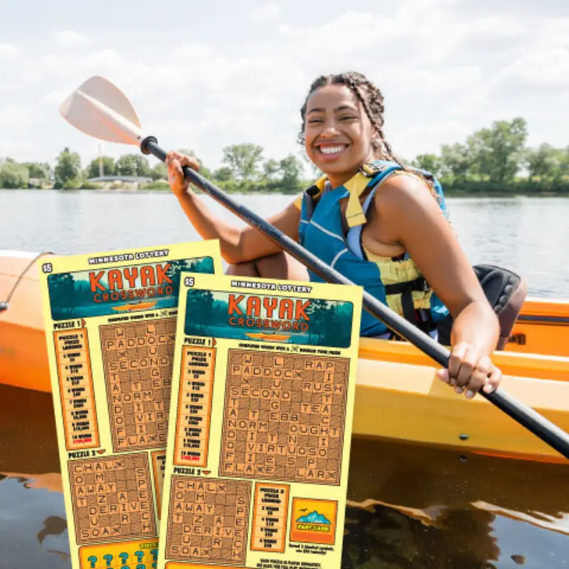 Smiling woman kayaking on a lake holds a paddle; two Minnesota Lottery Kayak Crossword tickets are shown in the foreground.