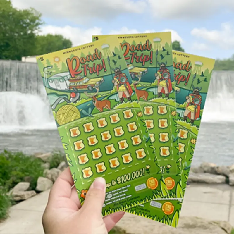 Hand holds three Road Trip! Minnesota Lottery scratch-off tickets before a waterfall, green trees, and blue sky.