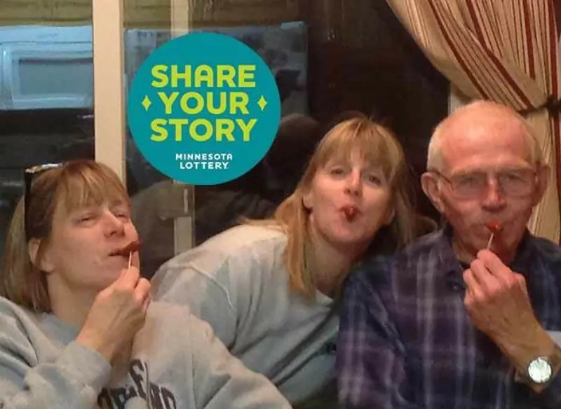 Three people indoors, enjoying food on a stick, pose playfully. Share Your Story Minnesota Lottery logo in the background. They express fun and camaraderie.