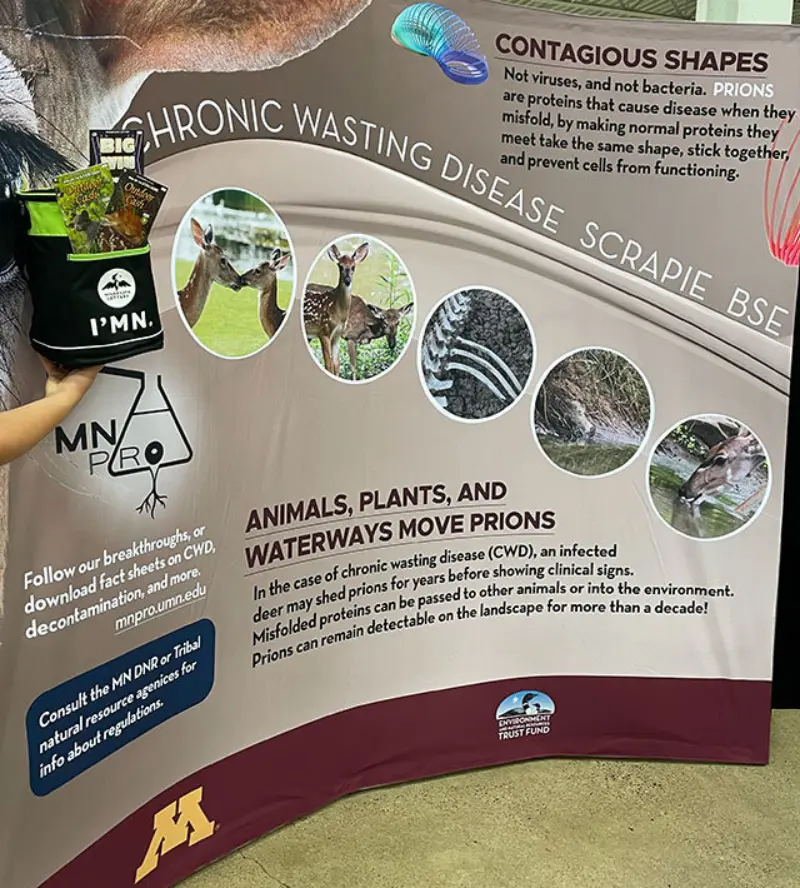 Chronic wasting disease booth with info, animal photos, a branded bag, and University of Minnesota plus trust logos at the bottom.